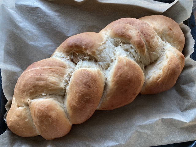 A 3-braid challah on a baking sheet, viewed from above.